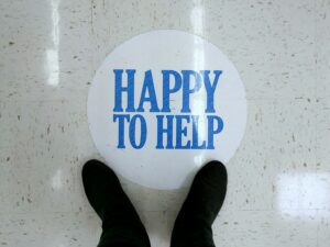 Feet in black boots looking at a sign on the floor of a store that says "Happy to Help."